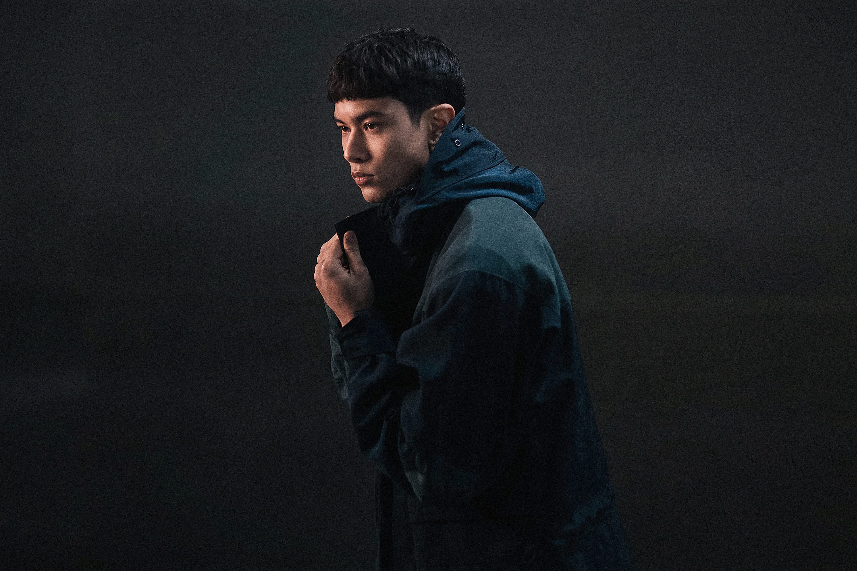 A founder in a dark hooded jacket, photographed in profile against a dark ground